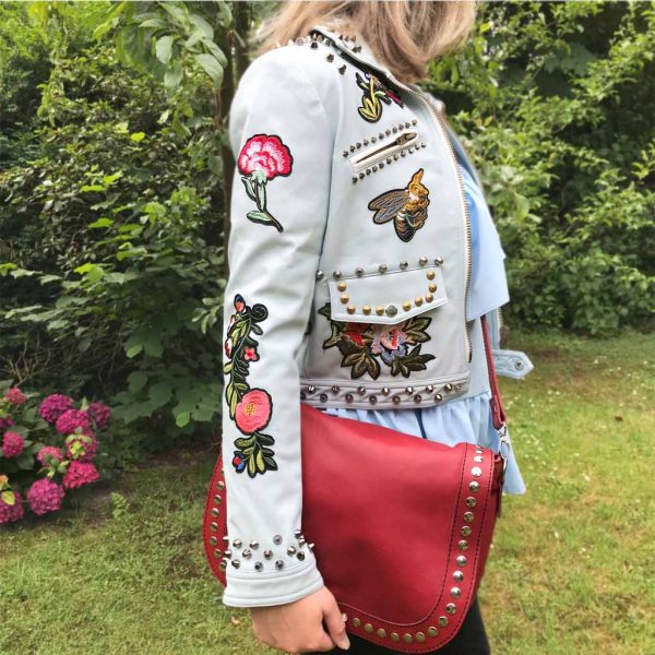Nevada Love Paris Kunst Lederjacke mit Nieten und Patches. Stickereien. Mit Reißverschlüssen. Hellblaue Leder Damenjacke in Große S 38. Im Outfit mit einer roten Ledertasche mit Nieten.