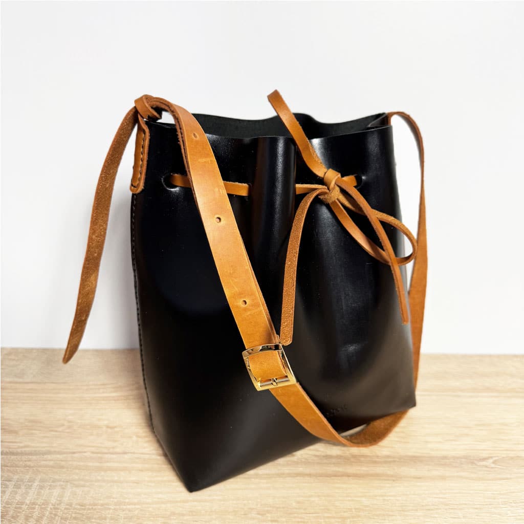 Zweifarbige Leder crossbody und Schultertasche schwarz mit cognacbraunem Riemen und Band. Mittelgroße Bucket bag mit einem längenverstellbaren, praktischen Riemen. Elegante. leichte Damen Ledertasche handgefertigt, geeignet für jeden Tag.